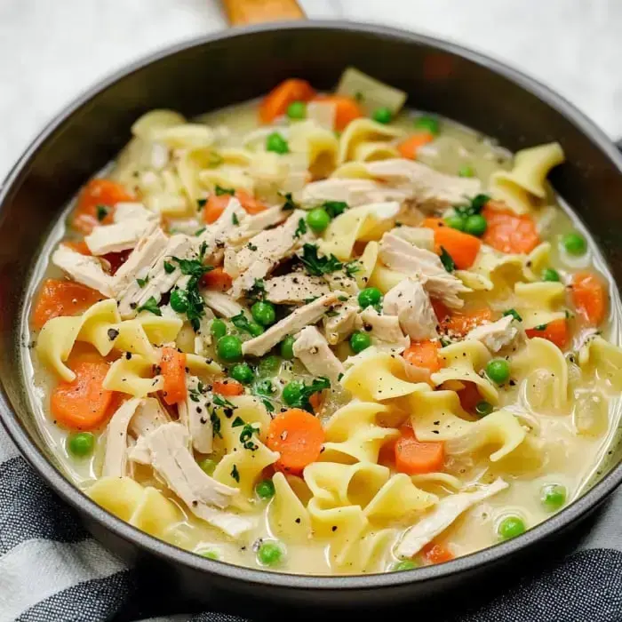 Close-up shot of creamy turkey noodle soup, featuring egg noodles, shredded turkey, diced carrots, and peas.