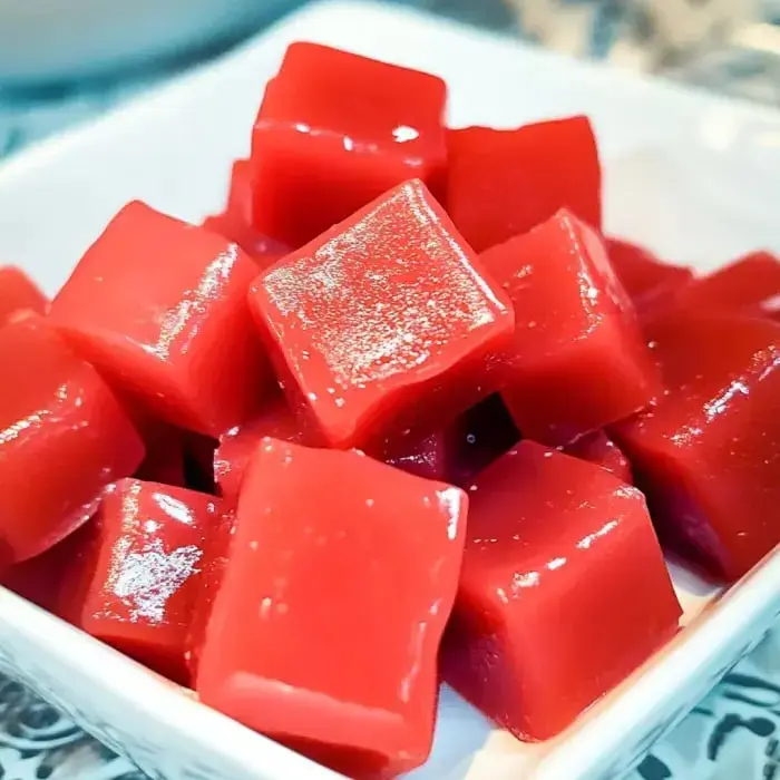 Close-up of shiny red candy squares stacked in a white dish.
