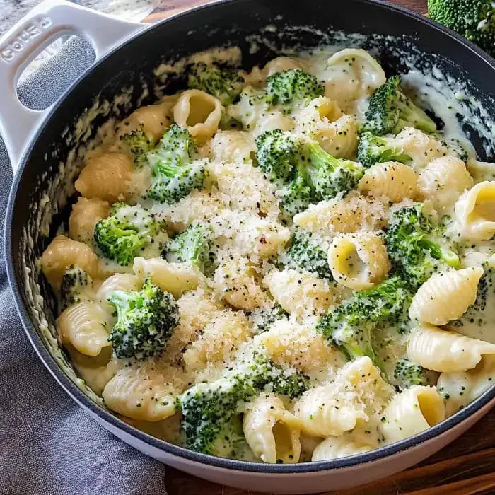 A pot of creamy broccoli pasta with shell pasta, sprinkled with cheese and black pepper.