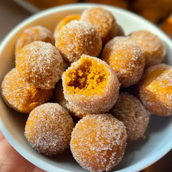 A bowl filled with orange, sugar-coated snack bites, with one missing a bite.
