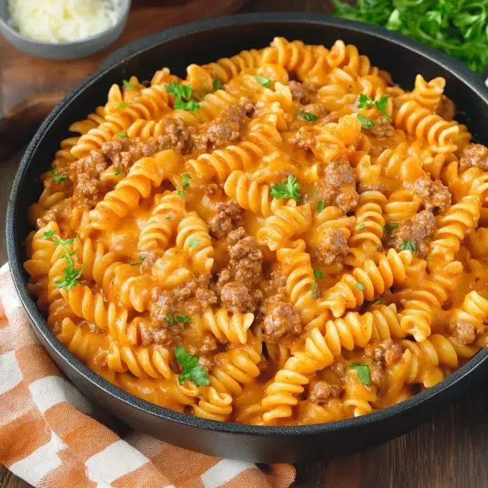 Close-up of spiral pasta in creamy tomato sauce with seasoned ground beef, topped with parsley.