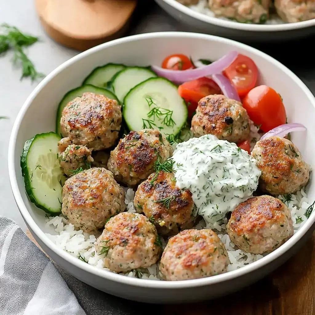Golden meatballs on rice with cucumbers, tomatoes, red onions, and creamy herb sauce on top.