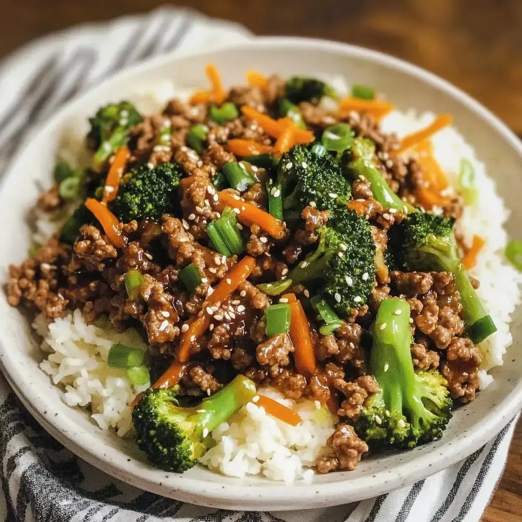 A serving of rice topped with fried beef, broccoli, carrots, and green onions, sprinkled with sesame seeds.
