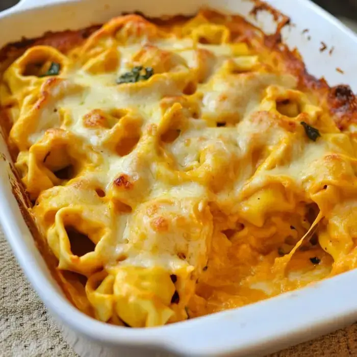 Baked tortellini dish in a creamy cheese sauce, topped with herbs.