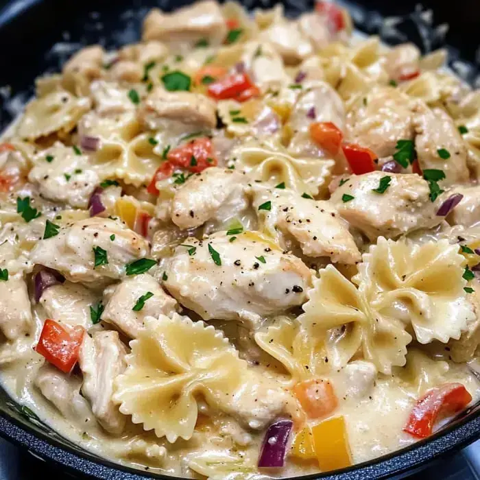 Close-up of creamy bow tie chicken pasta with vibrant veggies and fresh parsley garnish.