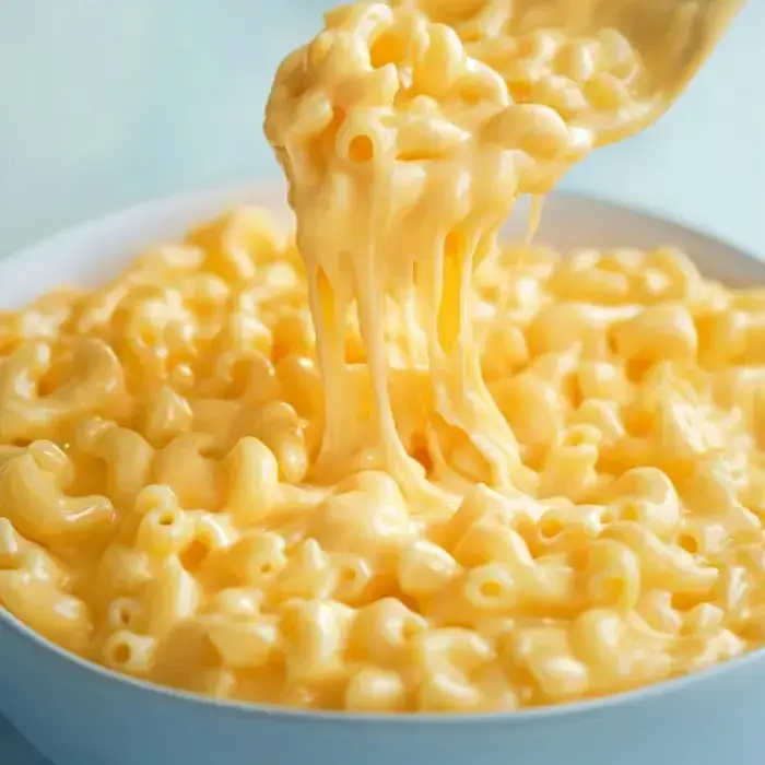 A spoon scooping up cheesy macaroni, showcasing its rich, stretchy texture in a creamy sauce.