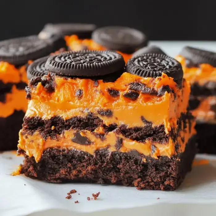 Close view of dessert layers with brownies, orange frosting, and Oreos on top.