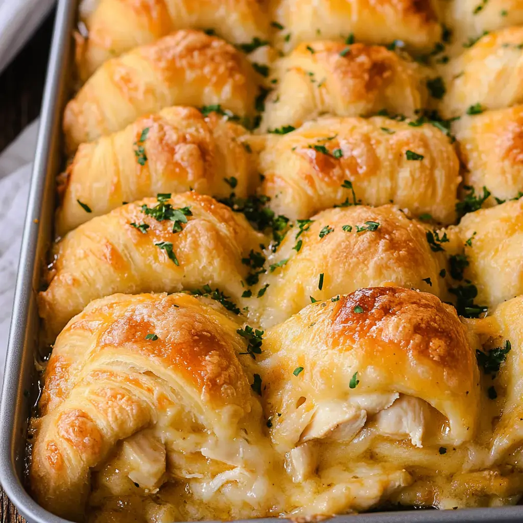Golden brown crescent rolls baked with gooey cheese and parsley, stacked in a dish.
