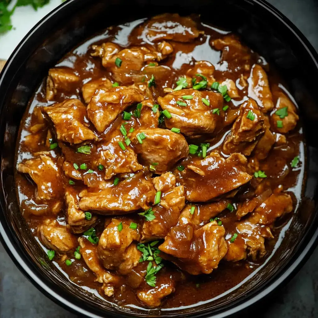 Pieces of tender chicken coated in a savory sauce, topped with fresh herbs, served in a bowl.