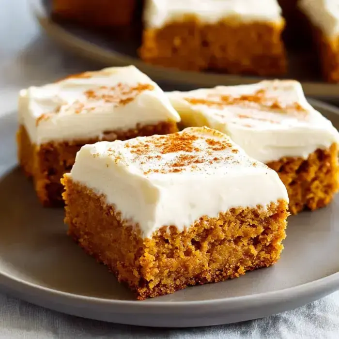 Pumpkin bars with frosting and a dusting of cinnamon on a plate.