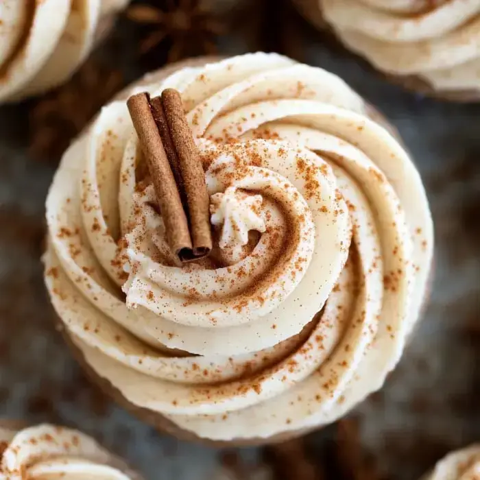 Close-up of frosted cupcake with cinnamon sticks and ground cinnamon on top.