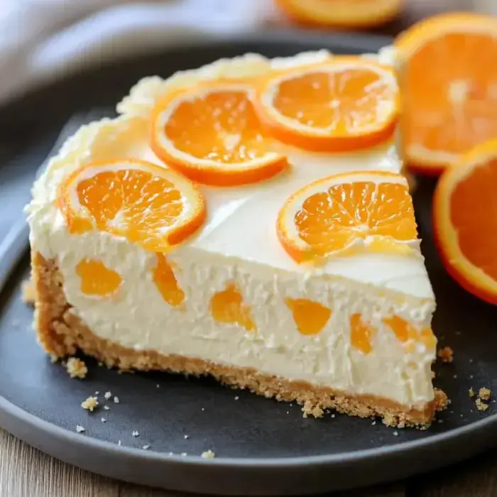 A creamy slice of orange cheesecake topped with mandarin slices on a dark plate.