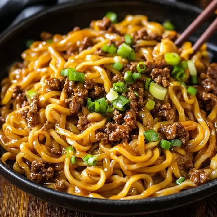 A bowl of noodles with savory ground meat and a sprinkle of chopped green onions.
