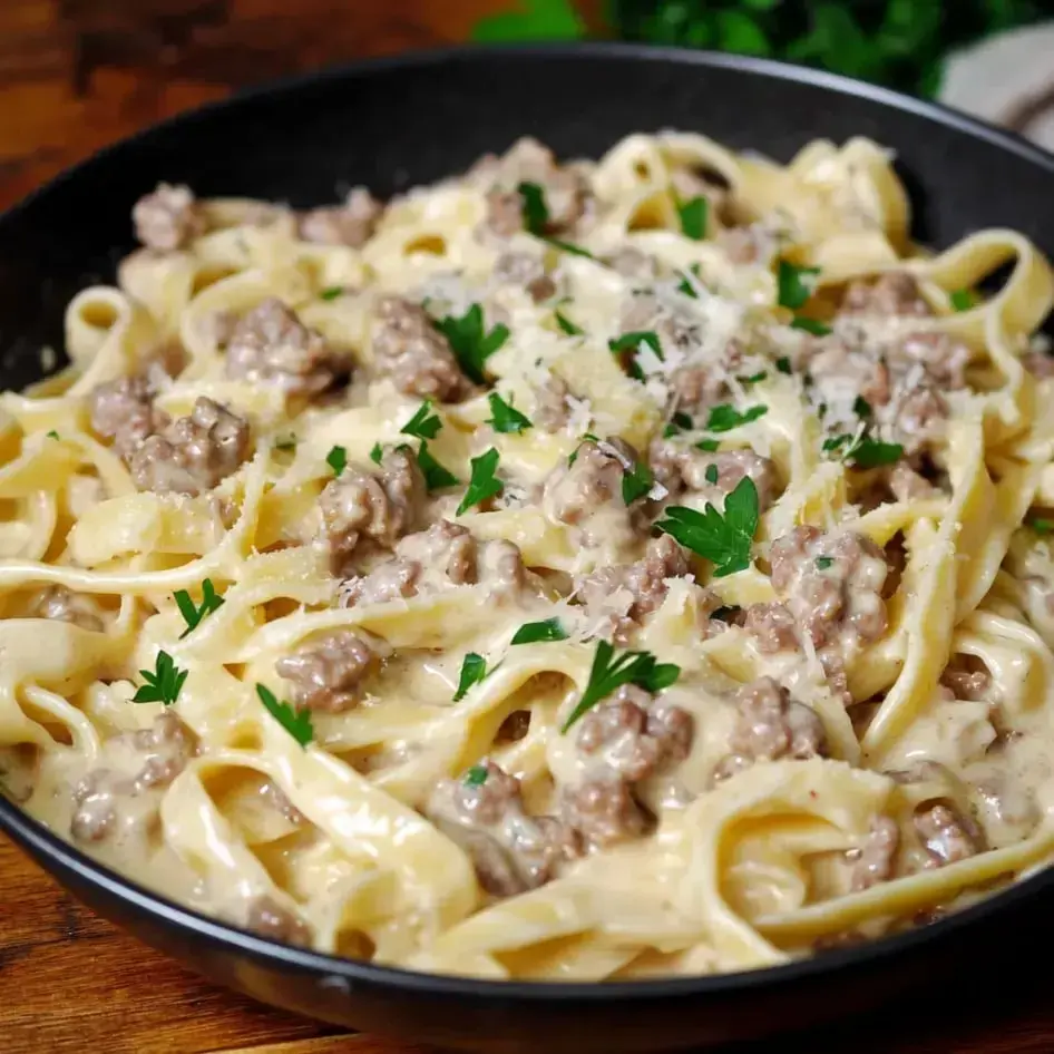 Bowl of creamy pasta with ground meat and parsley on top.
