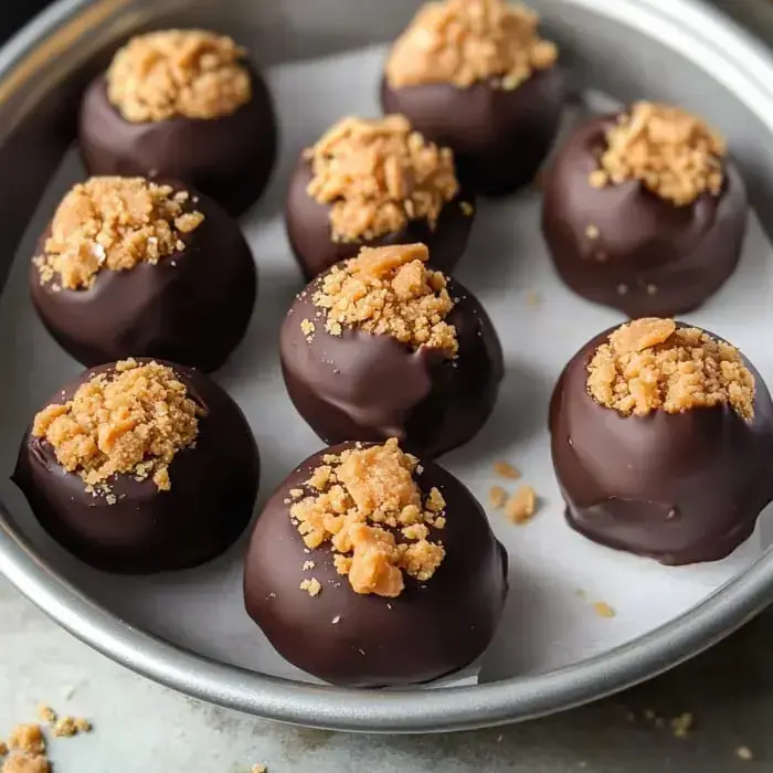 A silver plate with a bunch of chocolate-covered balls sprinkled with crushed cookies.