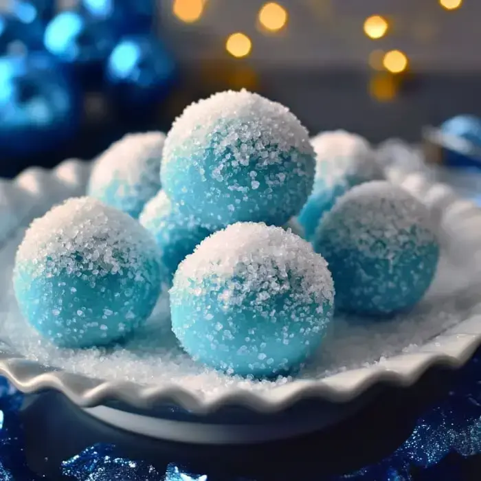 A festive plate of shimmery blue treats coated in sugar sits among sparkling blue ornaments with cozy, soft lighting in the background.