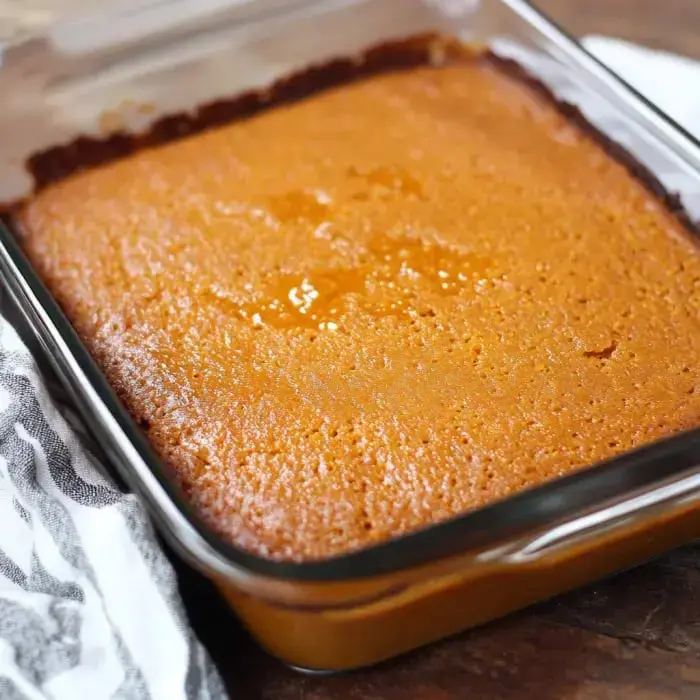 A golden cake just pulled from the oven sits in a clear dish on a wooden surface.