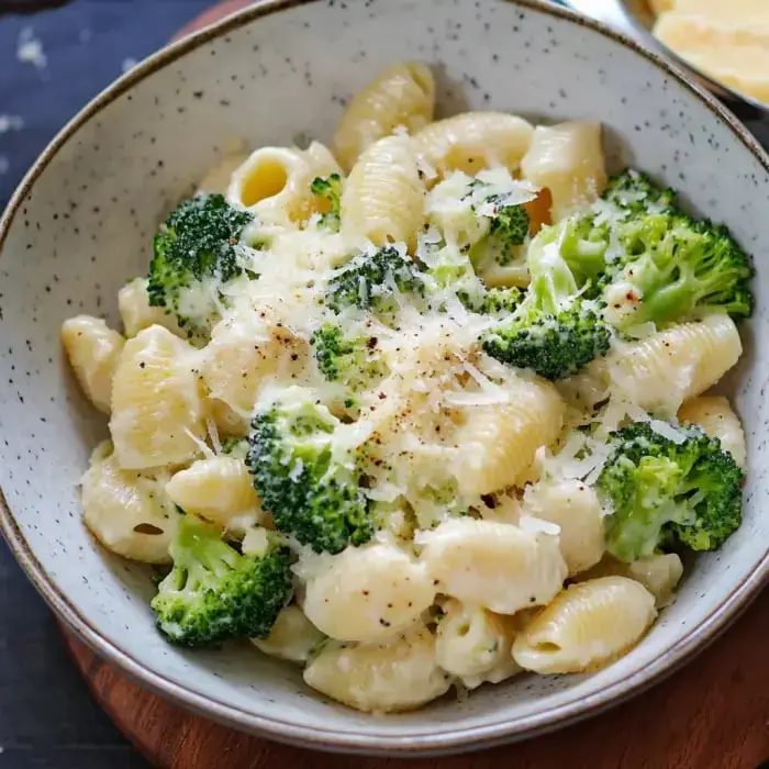 A bowl filled with creamy pasta and broccoli finished with shredded cheese on top.
