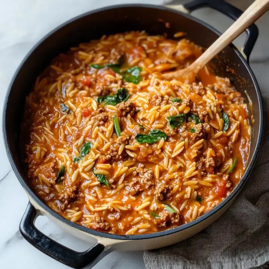 A big pot filled with creamy orzo, beef, spinach, and chunks of tomato.