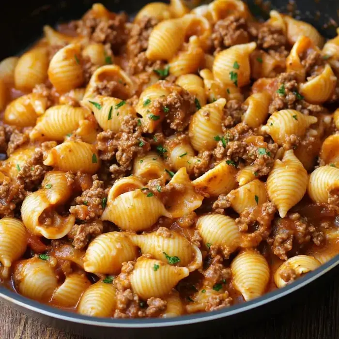 A skillet holding shell pasta and beef tossed in creamy tomato sauce and topped with chopped parsley.