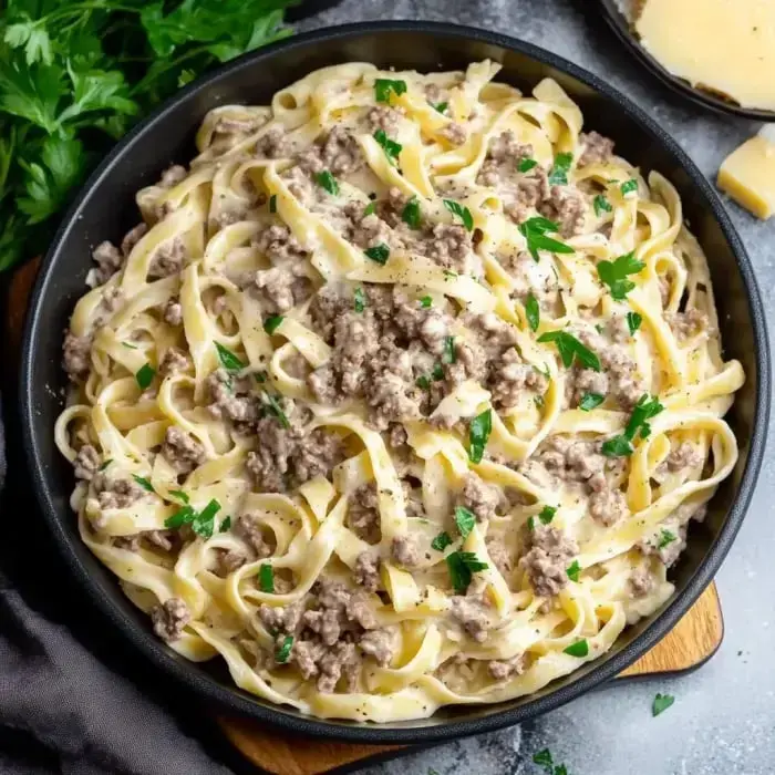 Creamy noodles in a bowl, topped with ground beef and fresh parsley for a finishing touch.