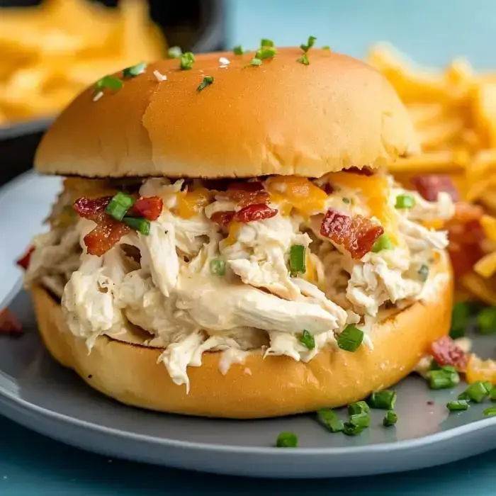 A shredded chicken sandwich loaded with green onions, bacon, and melty cheese, with fries on the side.