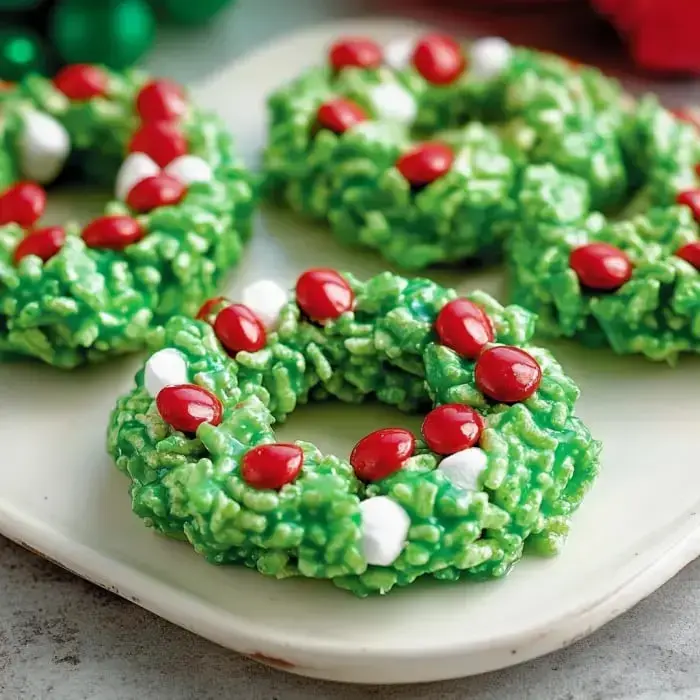 Festive green wreath-shaped treats stacked on a plate, topped with red candies and marshmallow bits.