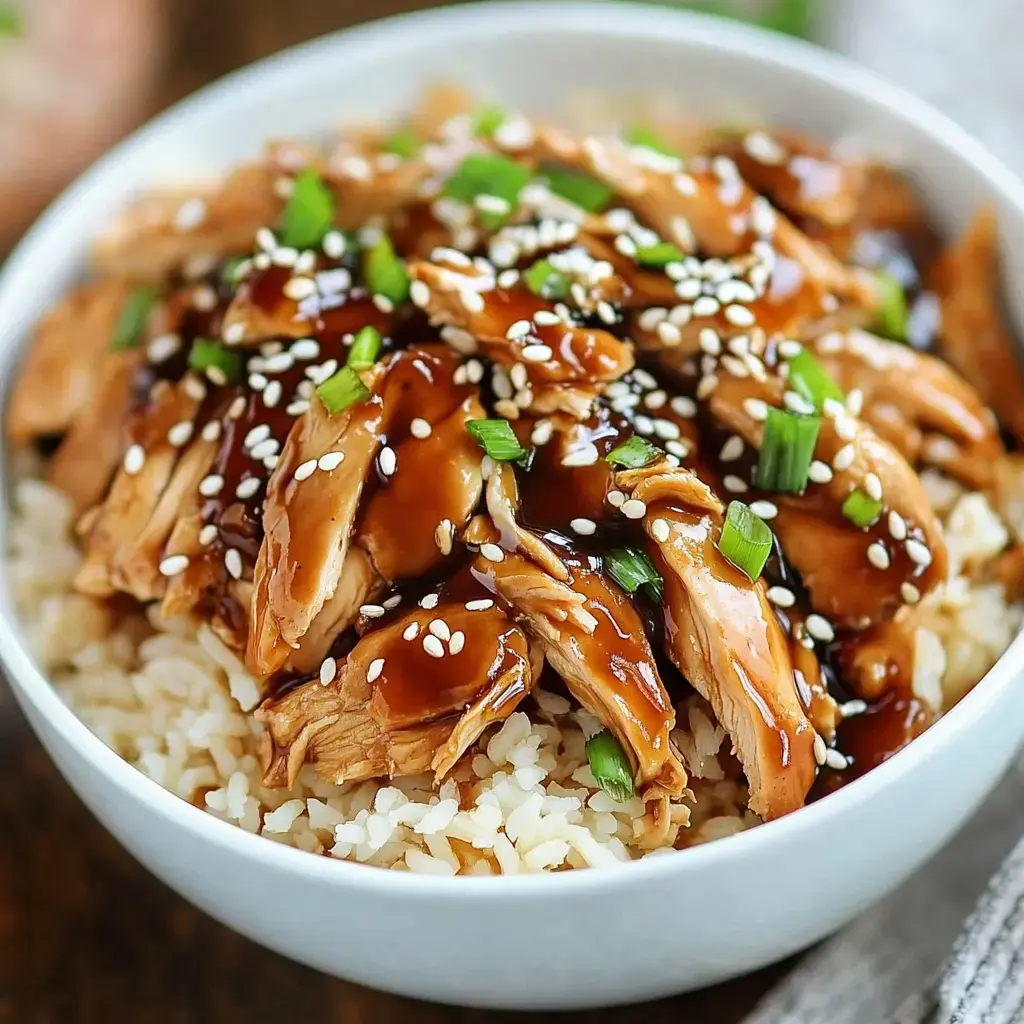 A closer look at rice in a bowl, topped with saucy sliced chicken, green onions and sesame sprinkled over.