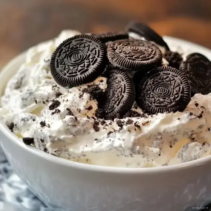 A bowl of fluffy whipped topping layered with chunks of Oreo cookies.