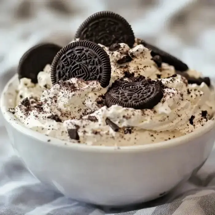 A bowl stacked high with whipped topping and big Oreo cookie pieces on top.