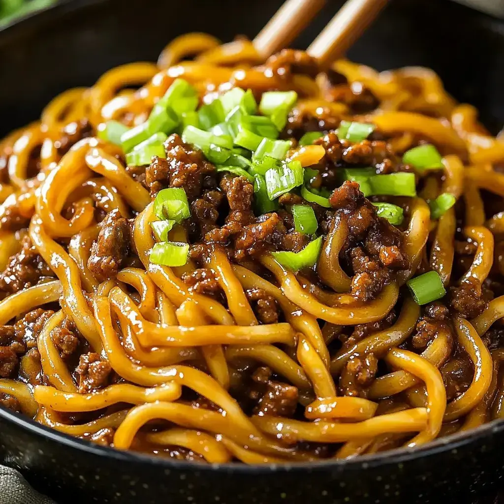 Steaming bowl packed with noodles ground beef and a sprinkle of fresh green onions on top.