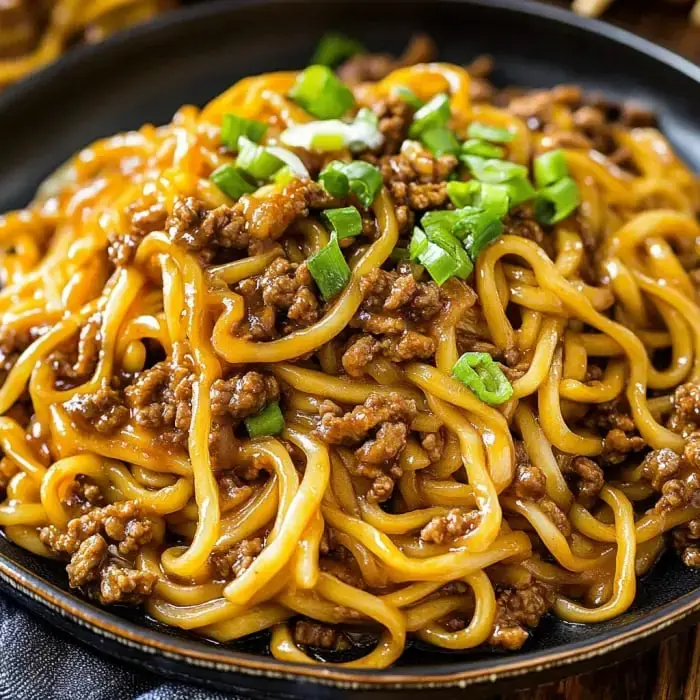 Plate of noodles loaded with savory ground beef bits and tossed with fresh green onion.