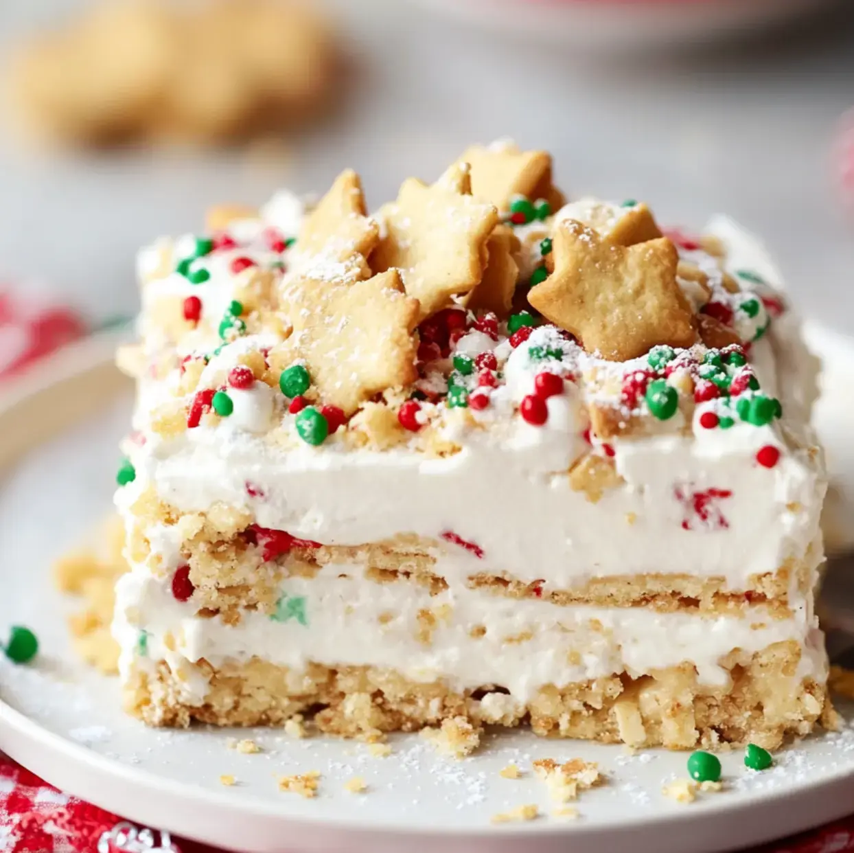 White plate with a slice of layered treat, fluffy topping, rainbow sprinkles, and fun cookies shaped like stars.