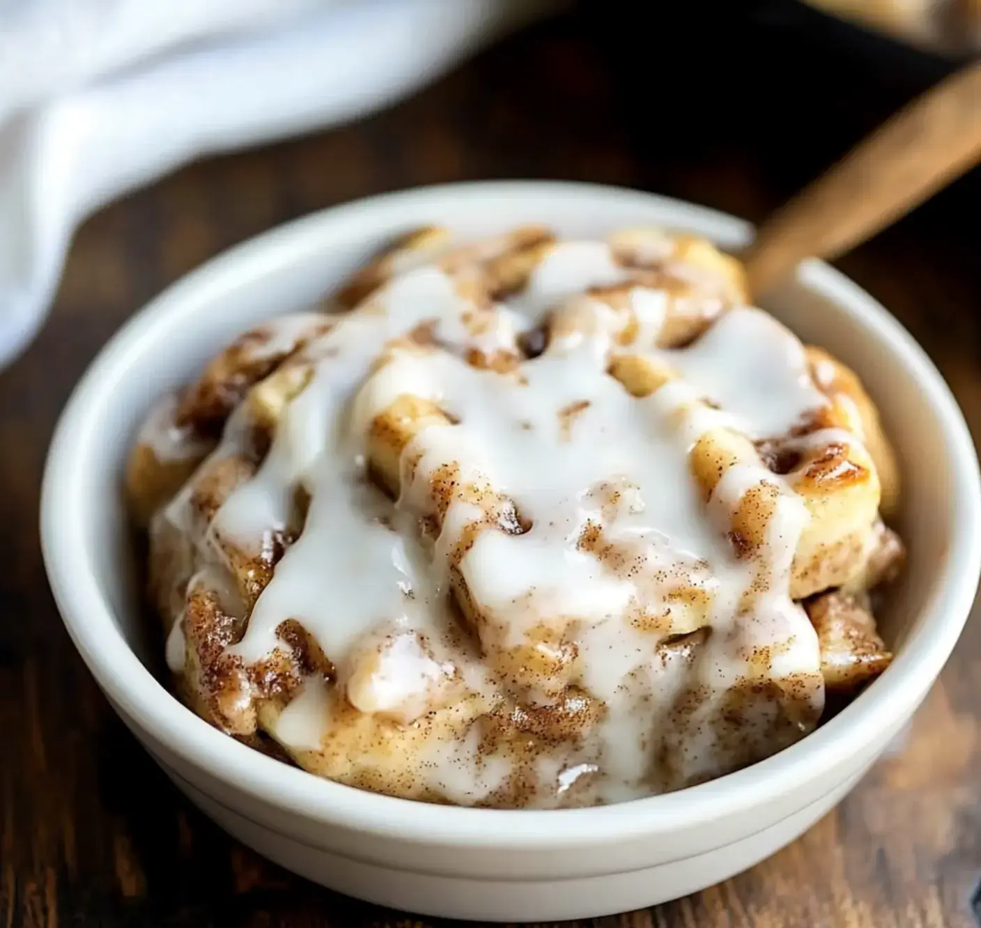 A bowl with cinnamon rolls and swirls of icing sitting on a wooden table.