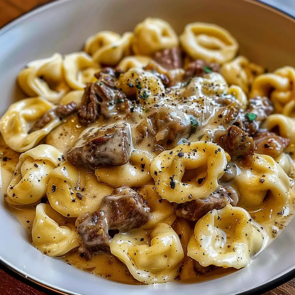 A creamy tortellini pasta dish with steak and spices served in a bowl.