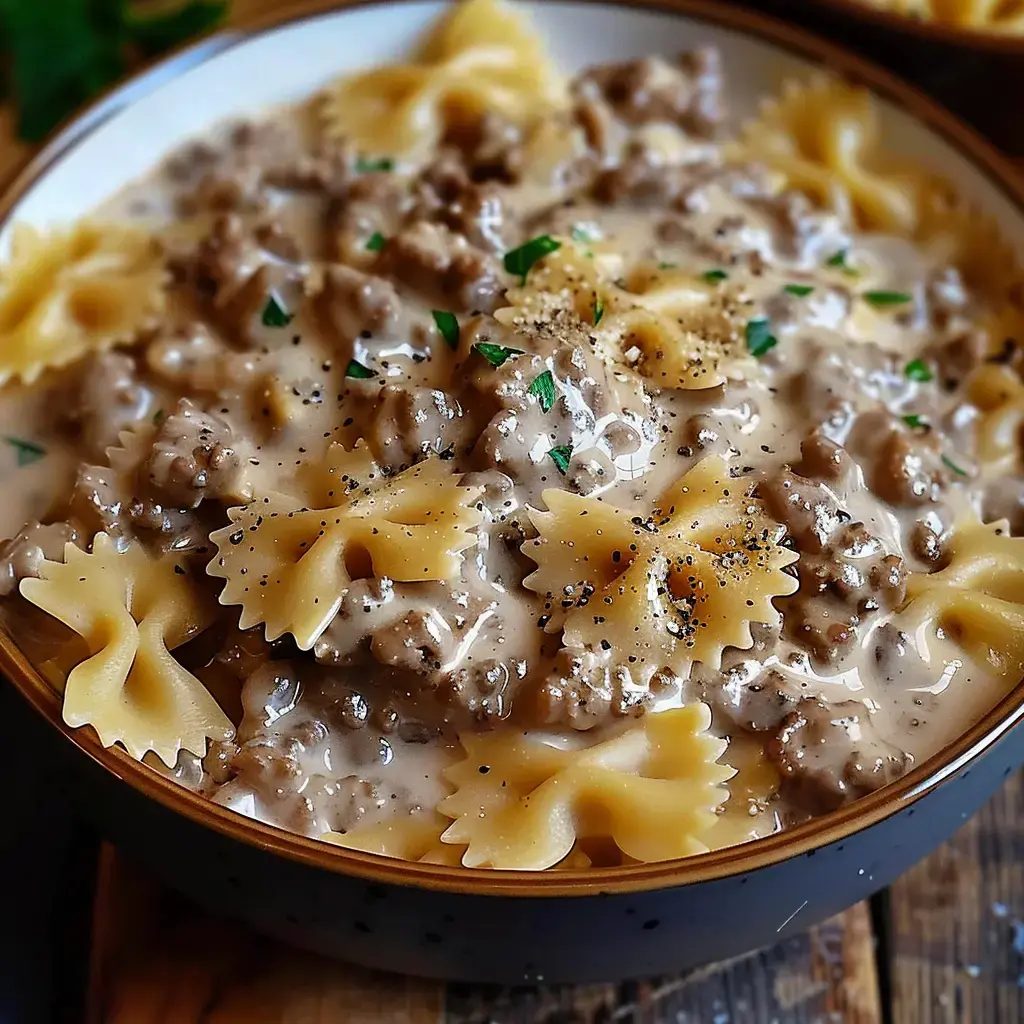 A bowl of bowtie pasta covered in a creamy meat sauce, sprinkled with pepper and fresh parsley.