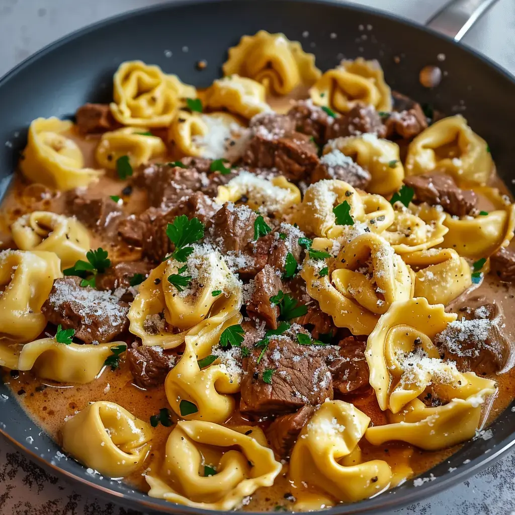 A creamy tortellini pasta dish served with chunks of beef, topped with parmesan and parsley.