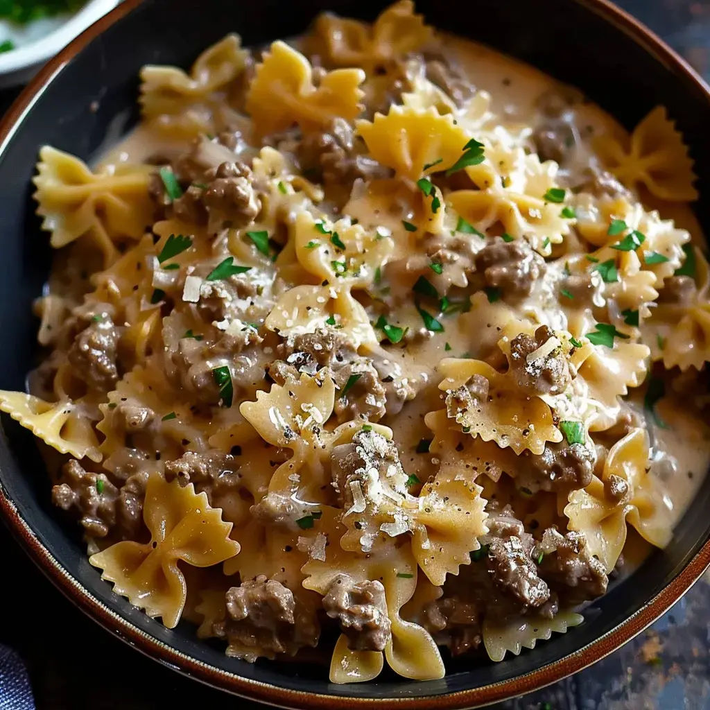 A bowl of butterfly-shaped pasta with ground meat in creamy sauce, topped with parsley.