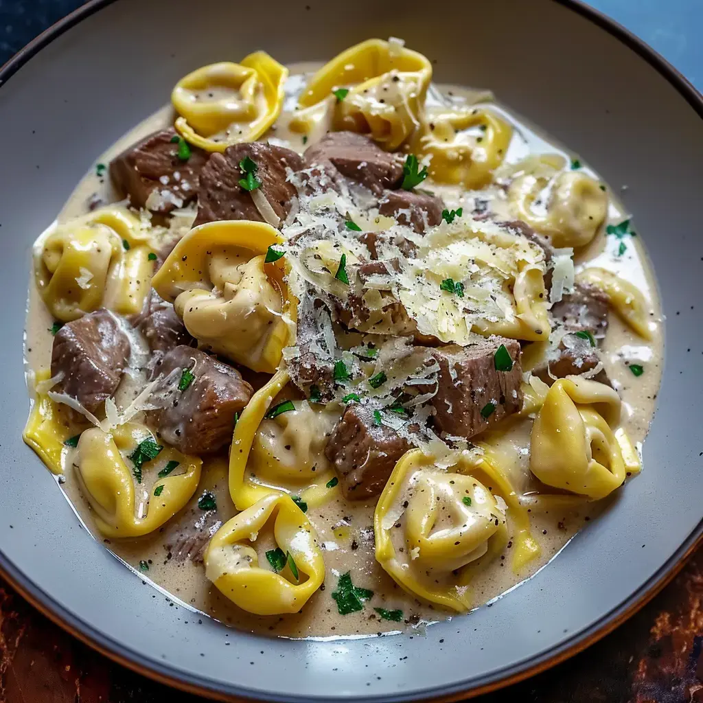 A plate of tortellini pasta with meat chunks in creamy sauce, topped with grated cheese and parsley.
