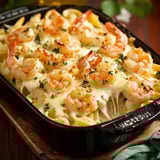 A black dish filled with creamy Alfredo pasta, shrimp, and melted cheese, ready to serve.