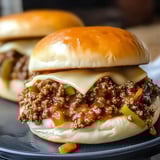 Two gooey sloppy joe sandwiches topped with cheese and diced green peppers on soft buns.