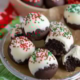 A platter of chocolate-dipped Oreo cookie balls with red and green sprinkles and white icing swirls.