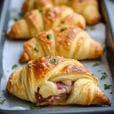 Golden crescent rolls stuffed with corned beef and cheese, sprinkled with parsley on a baking tray.