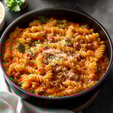 A pot full of creamy pasta spirals with ground beef, sprinkled with parsley and cheese on top.