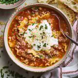 A cozy bowl of cheesy lasagna soup surrounded by crusty bread and fresh parsley.