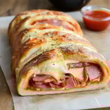 Crispy golden-brown stuffed bread, sliced to show ham, cheese, and marinara layers, served with a small dip bowl on the side.