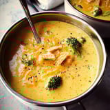 A bowl of cheddar broccoli soup topped with shredded cheese, crunchy croutons, and fresh pepper.