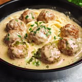 Creamy spaghetti topped with meatballs in a black bowl, garnished with parsley.