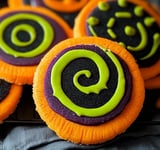 A close-up of vibrant Halloween cookies with colorful orange, green, and purple swirls of icing in fun patterns.