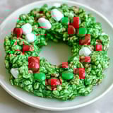 Green cornflake wreath decorated with candies and marshmallows on a plate.
